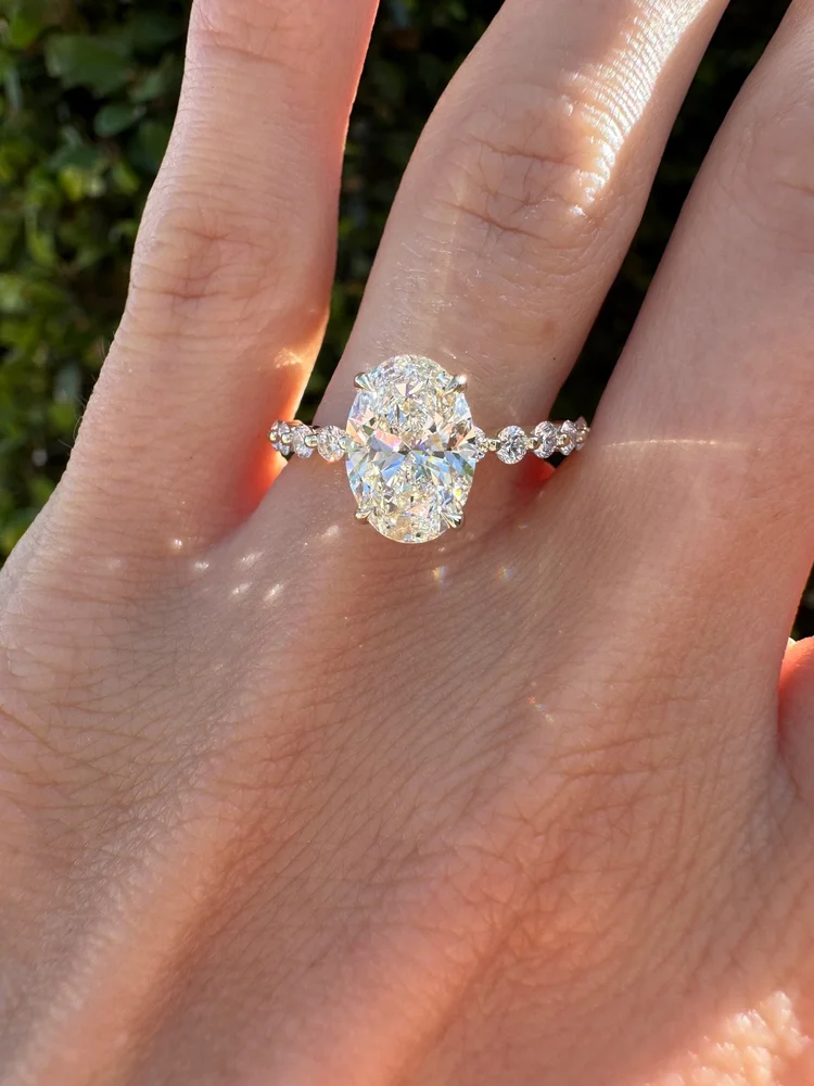Oval diamond solitaire on a thin band set with spaced round diamonds