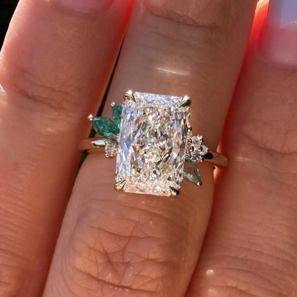 Custom-cut radiant diamond engagement ring with softened corners, round diamonds and marquise green emerald side stones