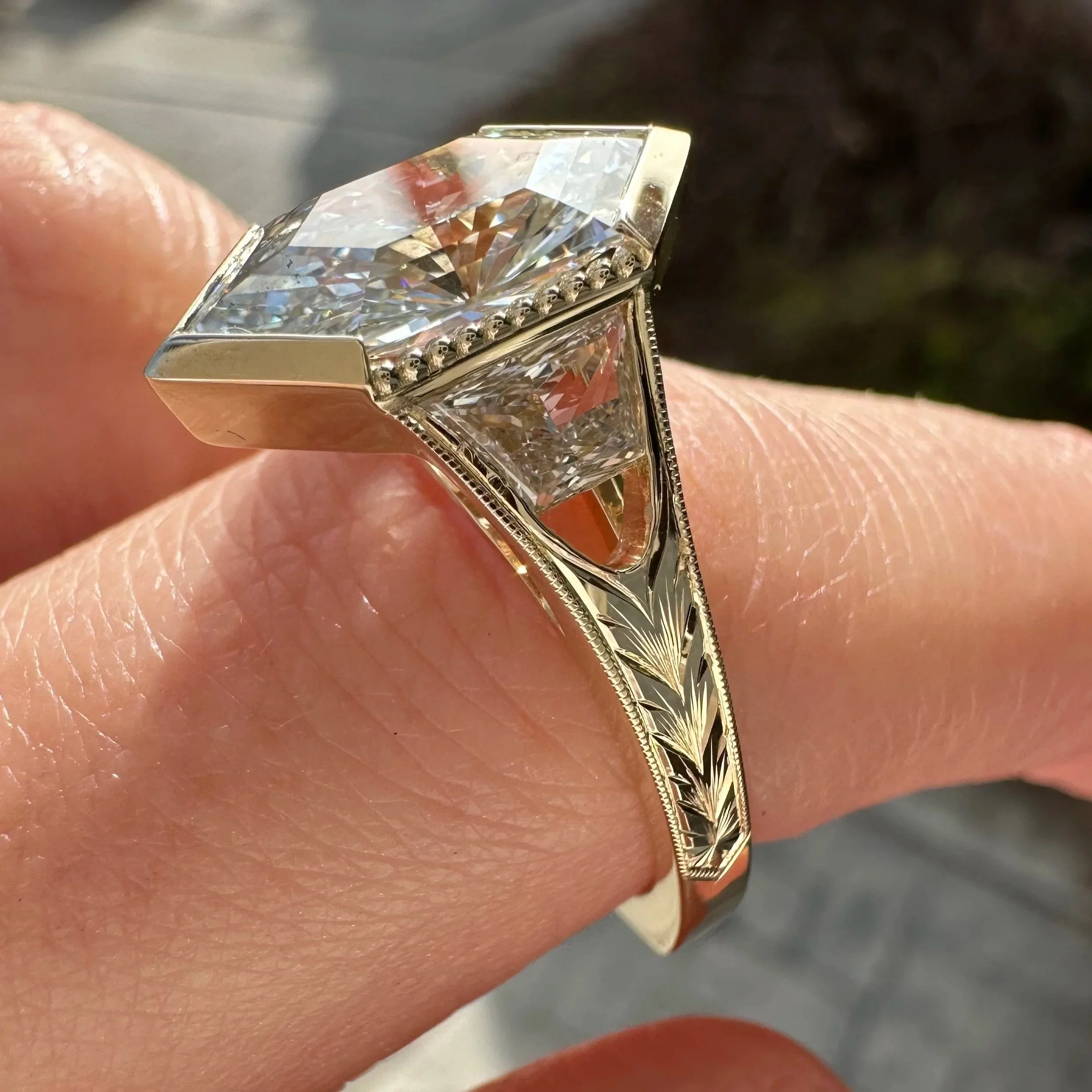Close-up of a kite-shaped diamond ring with an engraved yellow gold band