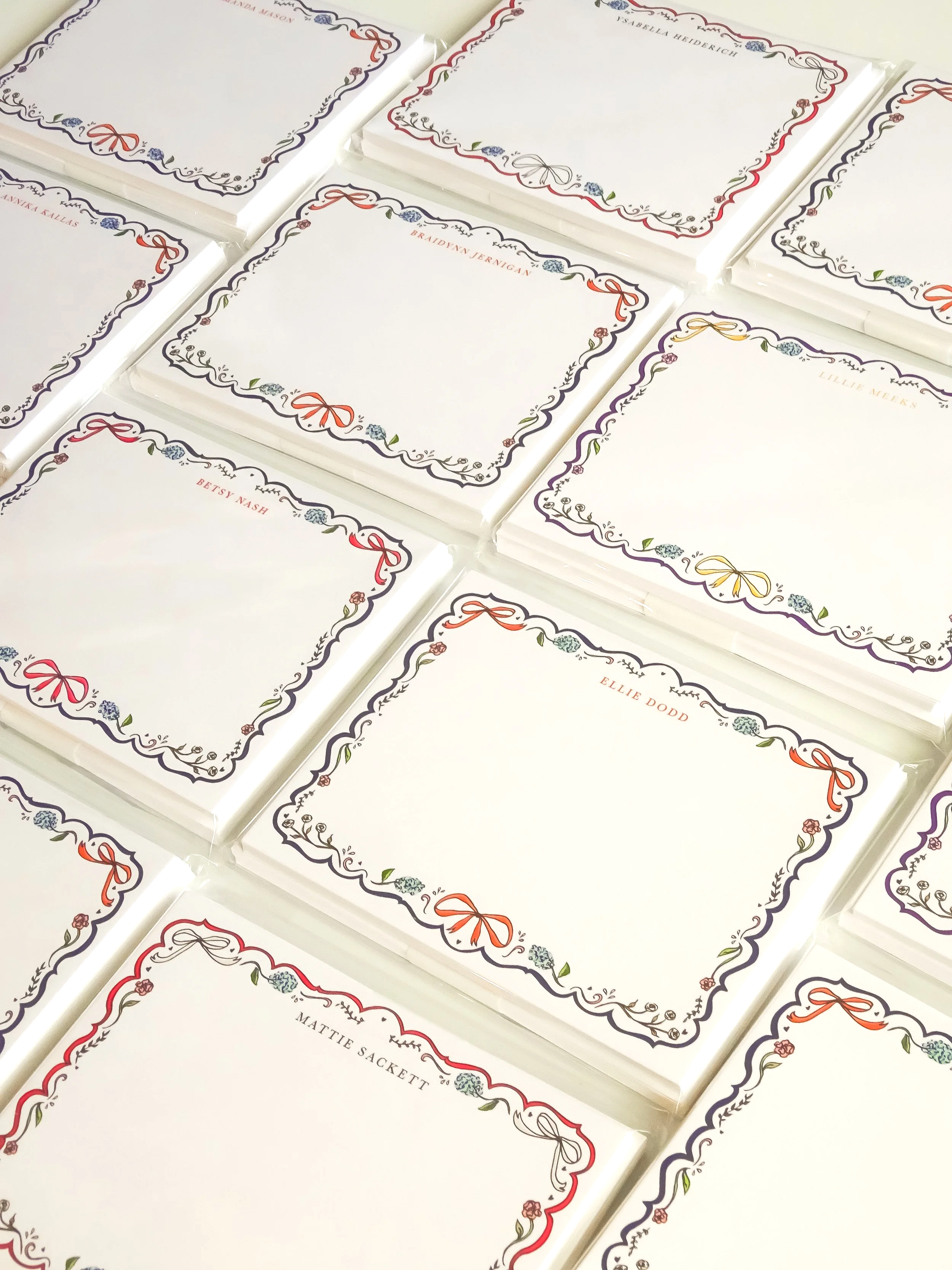 Multiple white vouchers or cards with decorative floral borders and rounded corners, each featuring a name printed in the center, including names like Betsy Nash, Mattie Sackett, Ellie Dodd, Braidyn Jernigan, Isabella Heiderich, and others.