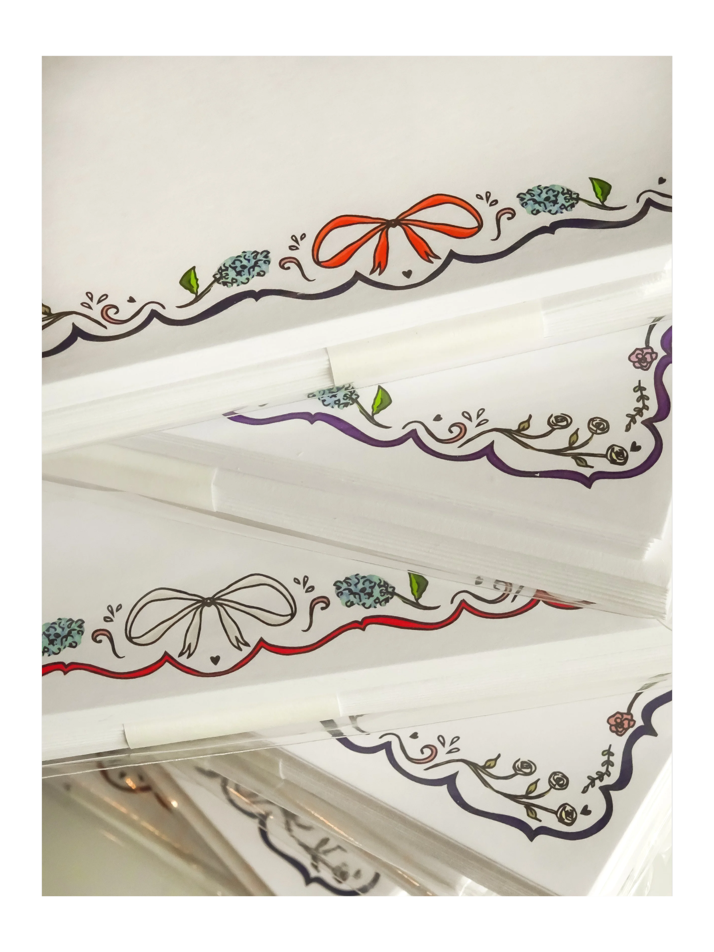 Decorative paper with a border design of flowers, leaves, a bow, and small hearts.