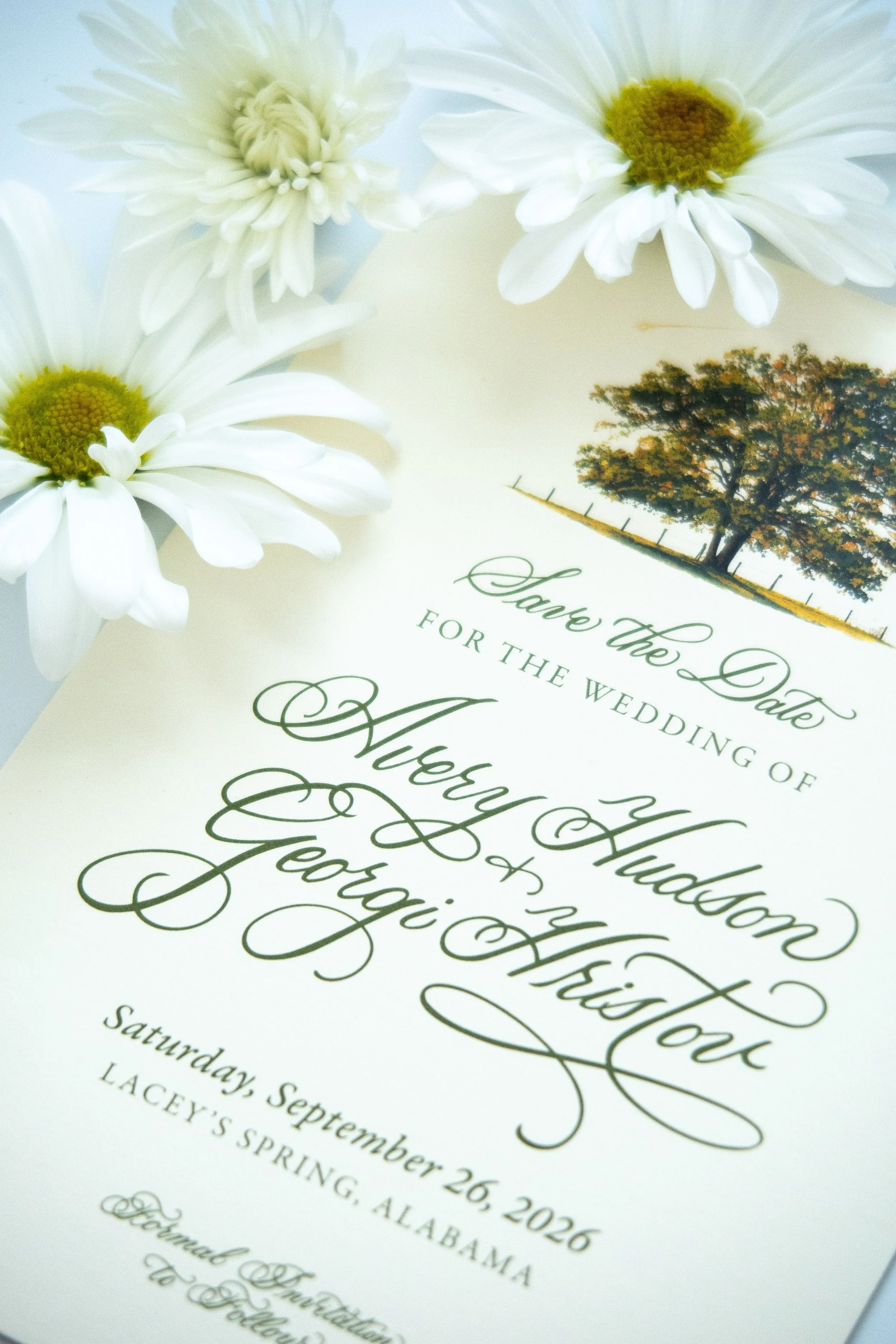 A wedding invitation with cursive black text and floral decorations, featuring white daisies and a tree.