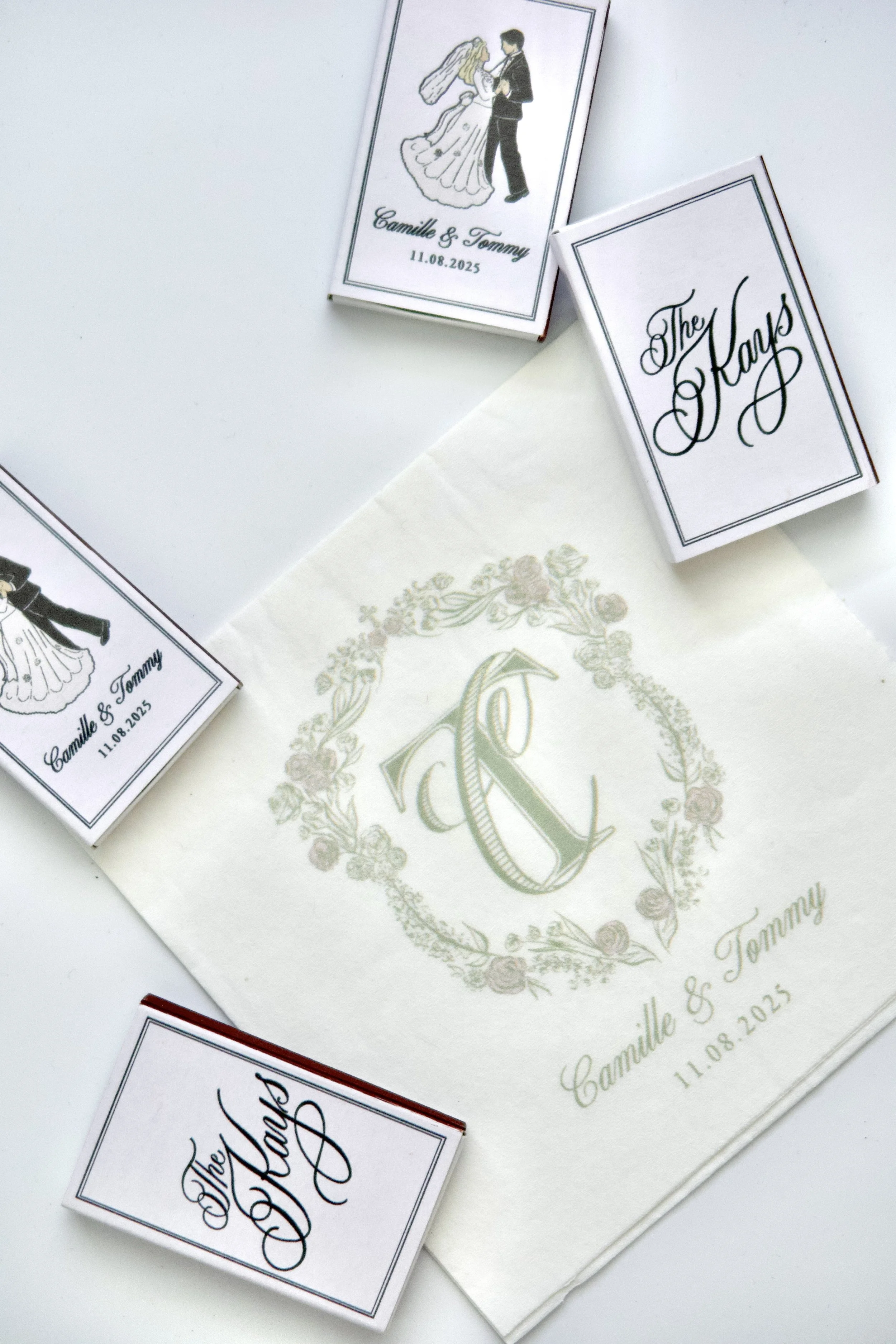 Wedding matchboxes and a napkin, with the names Camille & Tommy and the date 11.08.2025. The cards feature illustrations of a bride and groom and elegant script text.