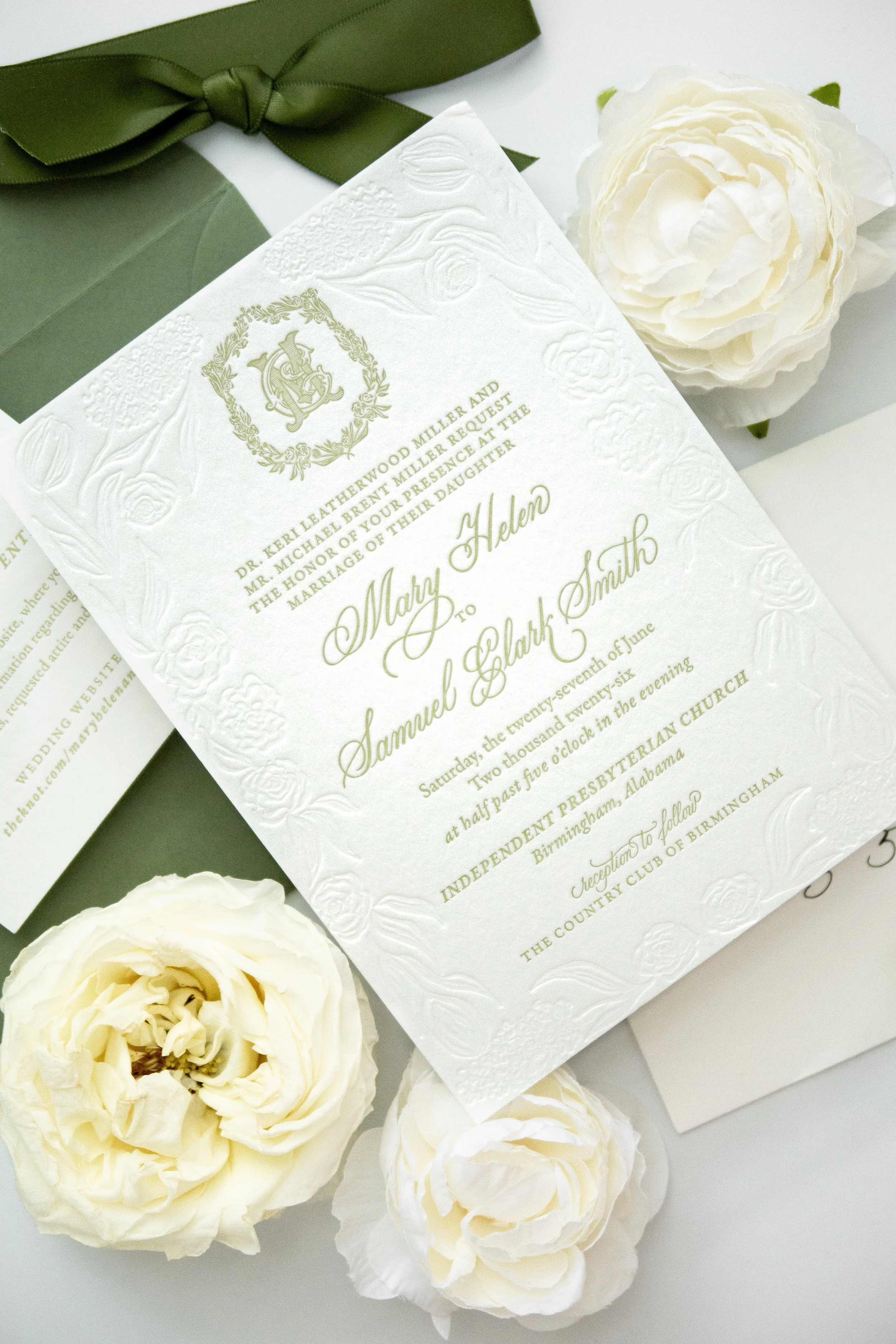 Wedding invitation with embossed details, a white rose, and a green ribbon.