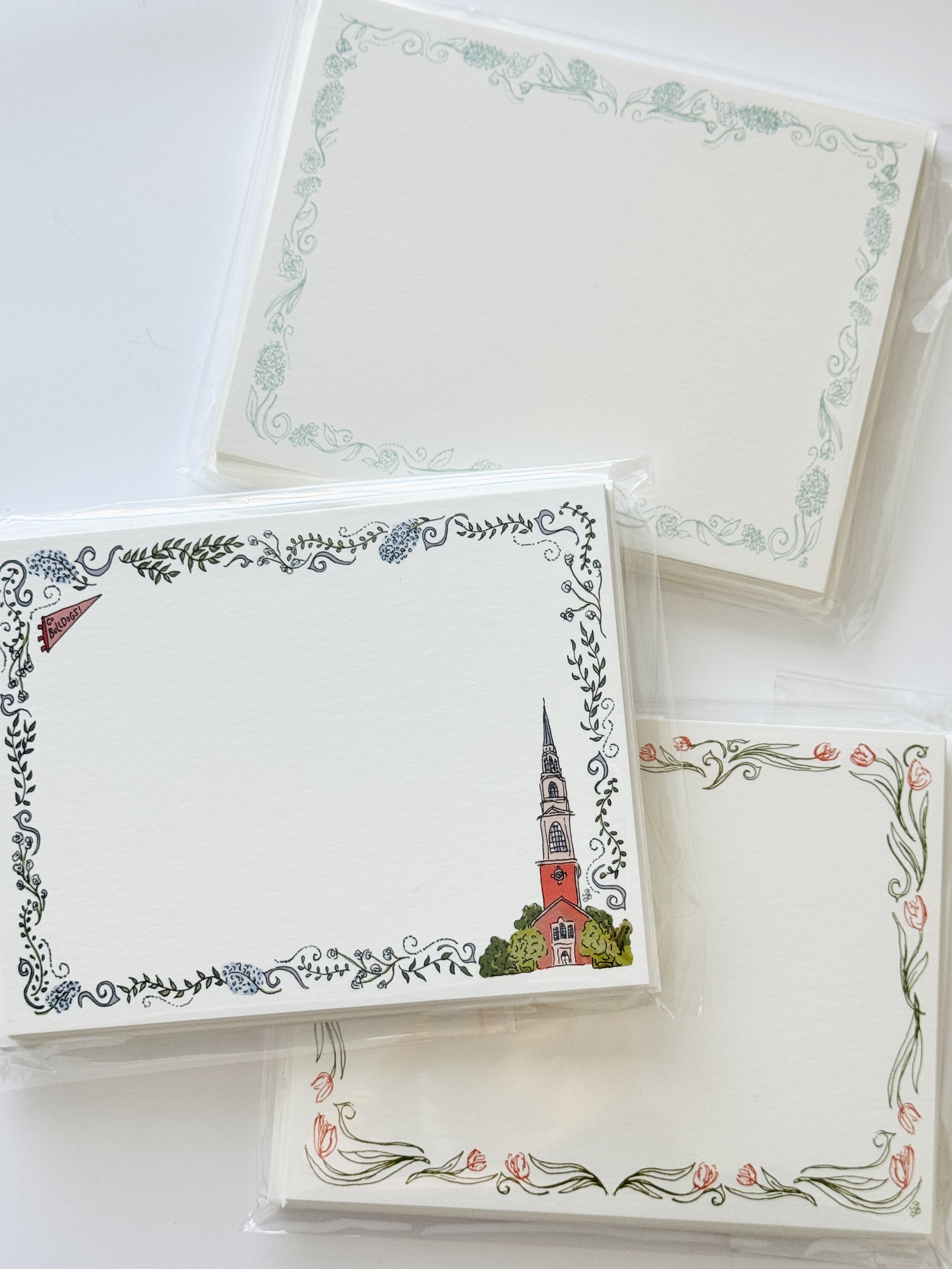 A set of decorative blank cards with floral borders, one featuring an illustration of a church steeple and building, in a clear plastic bag.
