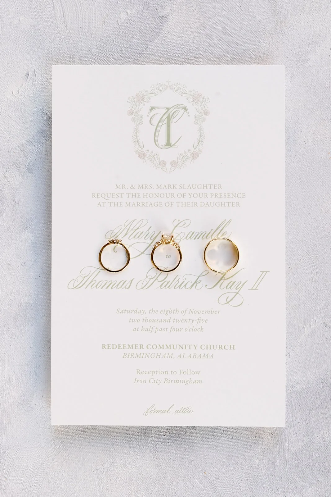 Wedding invitation card with three gold rings placed on it, featuring ornate floral design and elegant script text.