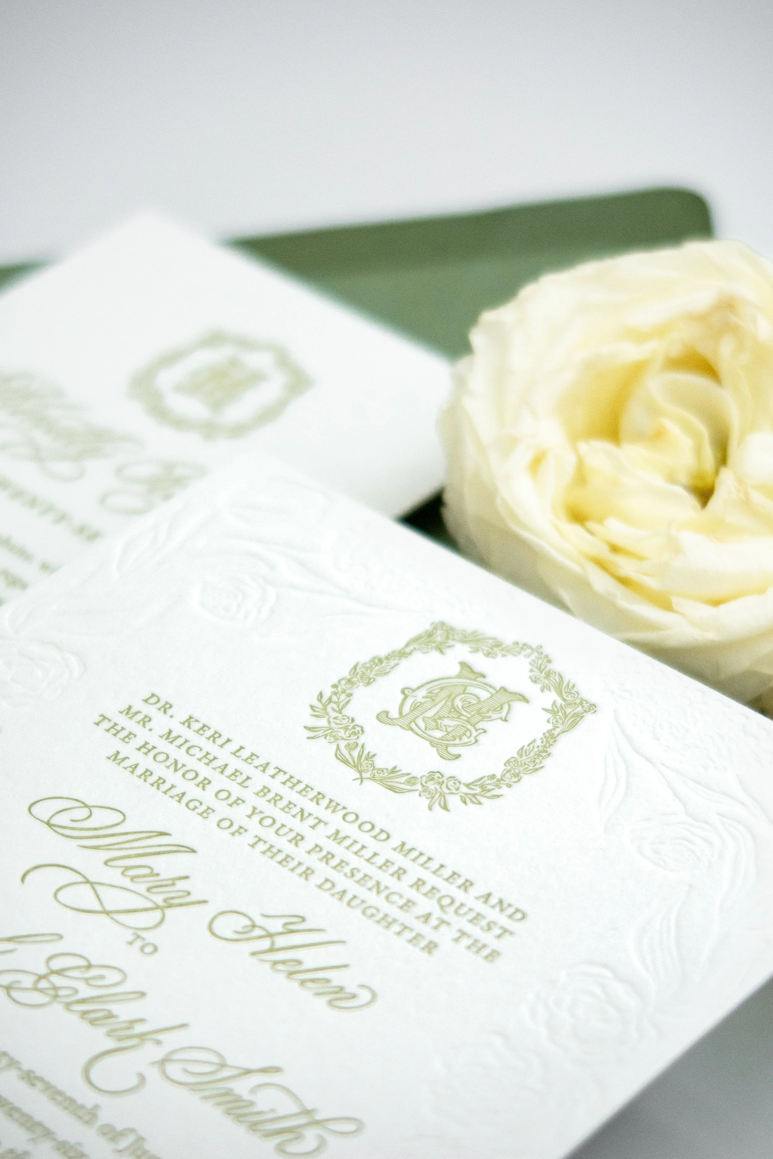 An invitation with elegant gold and green design for a wedding, featuring a white rose.