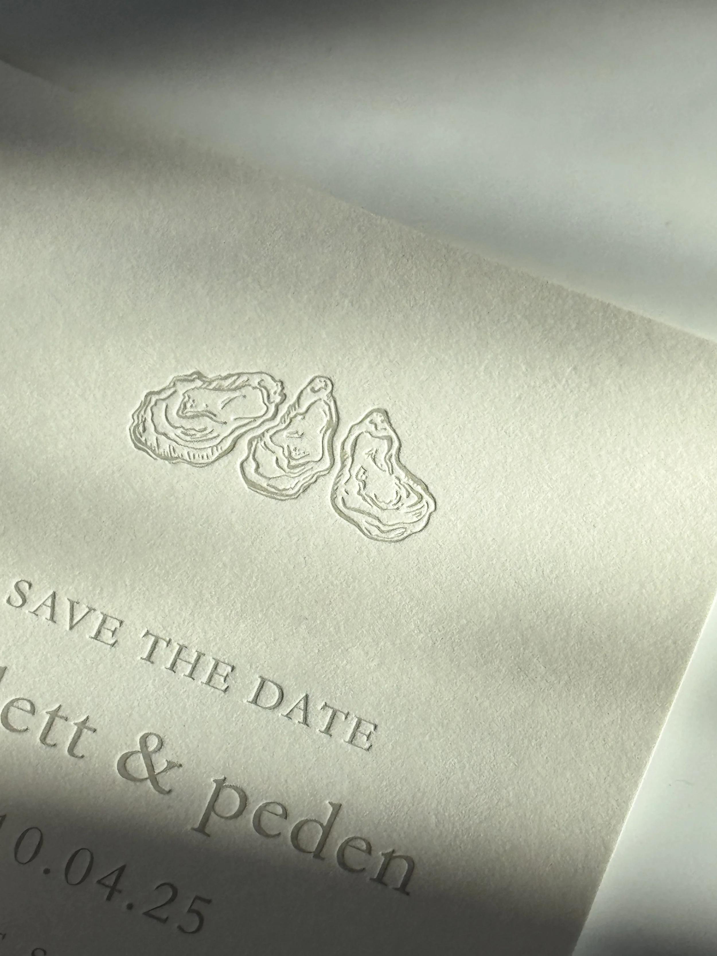 Close-up of embossed images of three oysters and partial text on a light-colored paper.