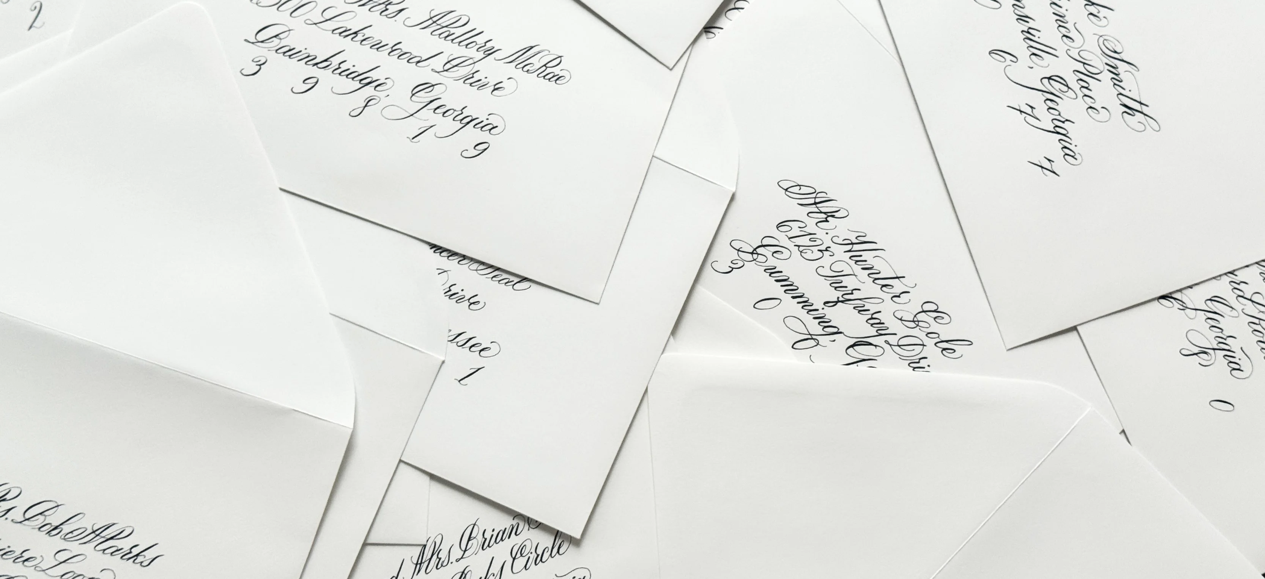 Multiple white envelopes with handwritten calligraphy addresses by Bella Taylor scattered on a flat surface.
