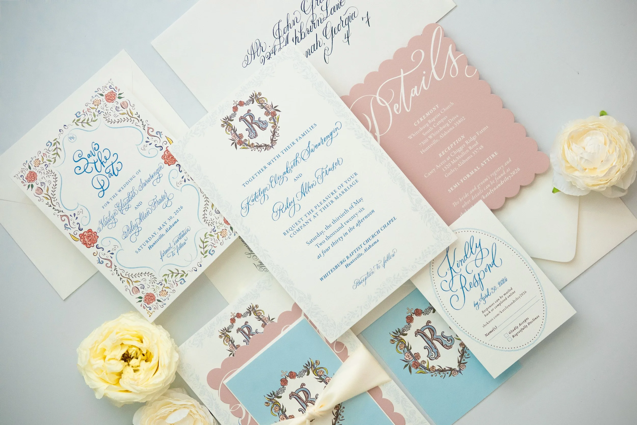 Close-up view of various wedding invitations with elegant script and floral designs, accompanied by cream-colored ranunculus flowers.