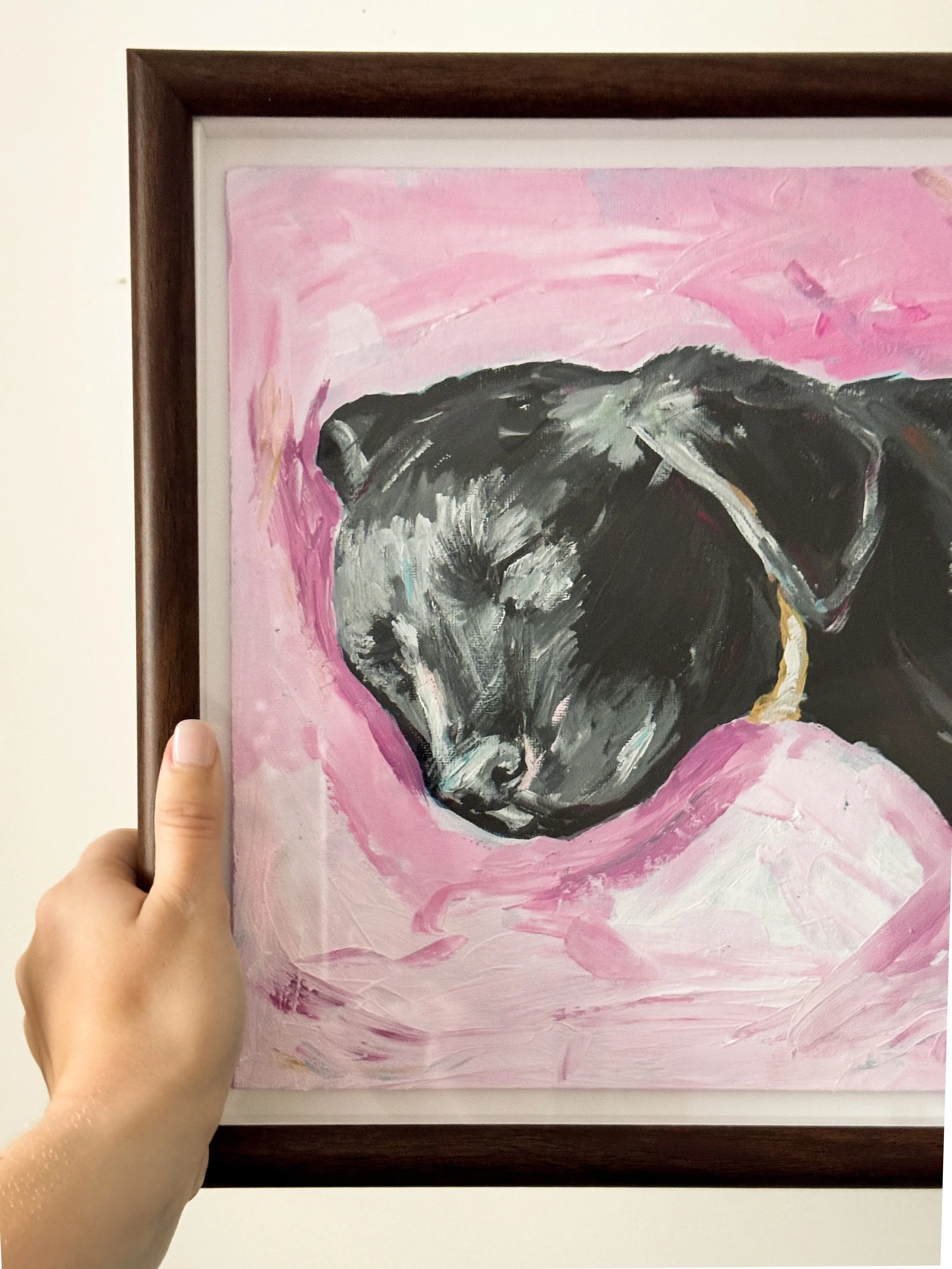 A painting of a black puppy's face on a pink background, framed in dark wood.