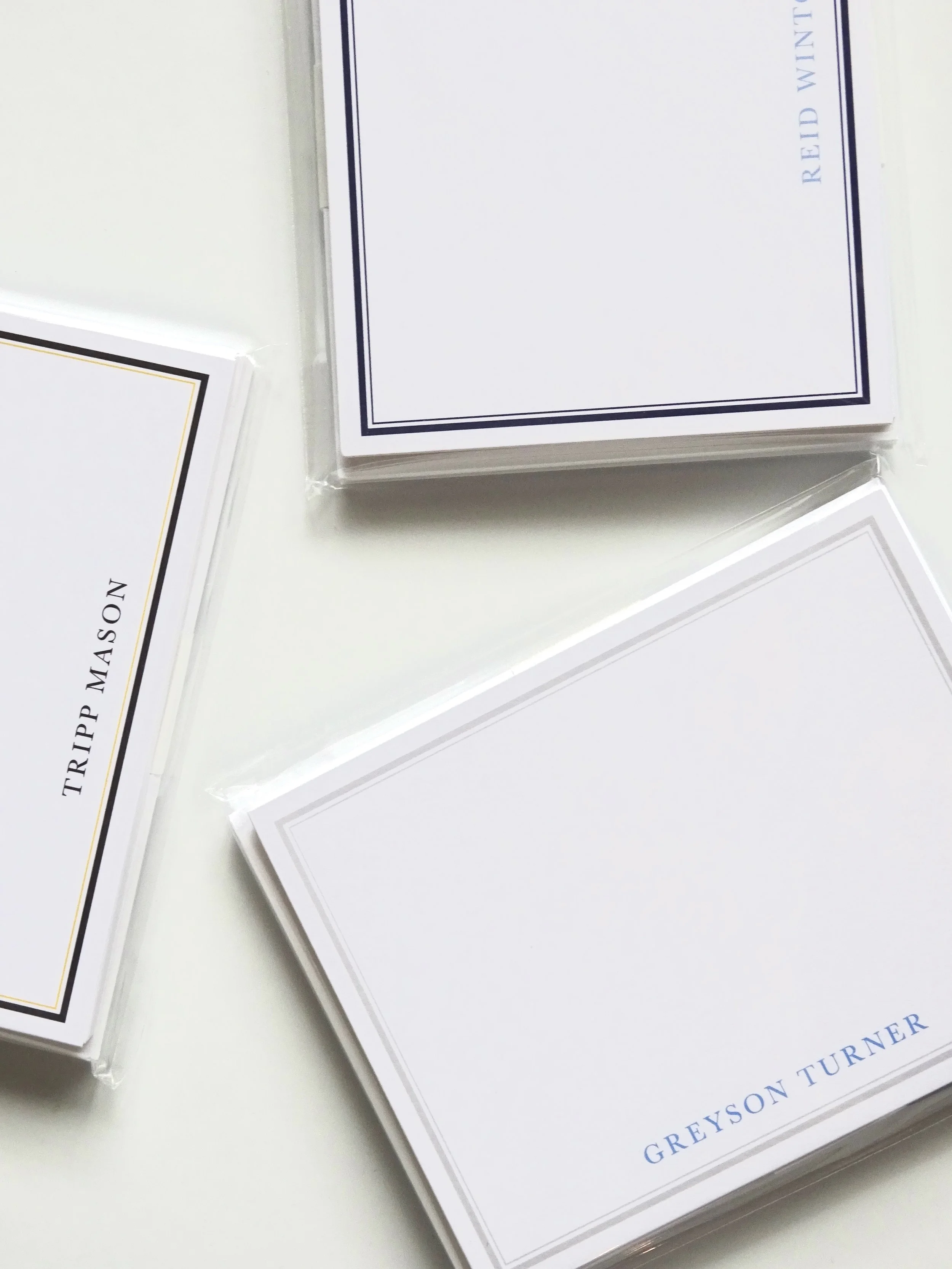 Stacks of white business cards with a black and gold border, and blue text, placed on a white surface.