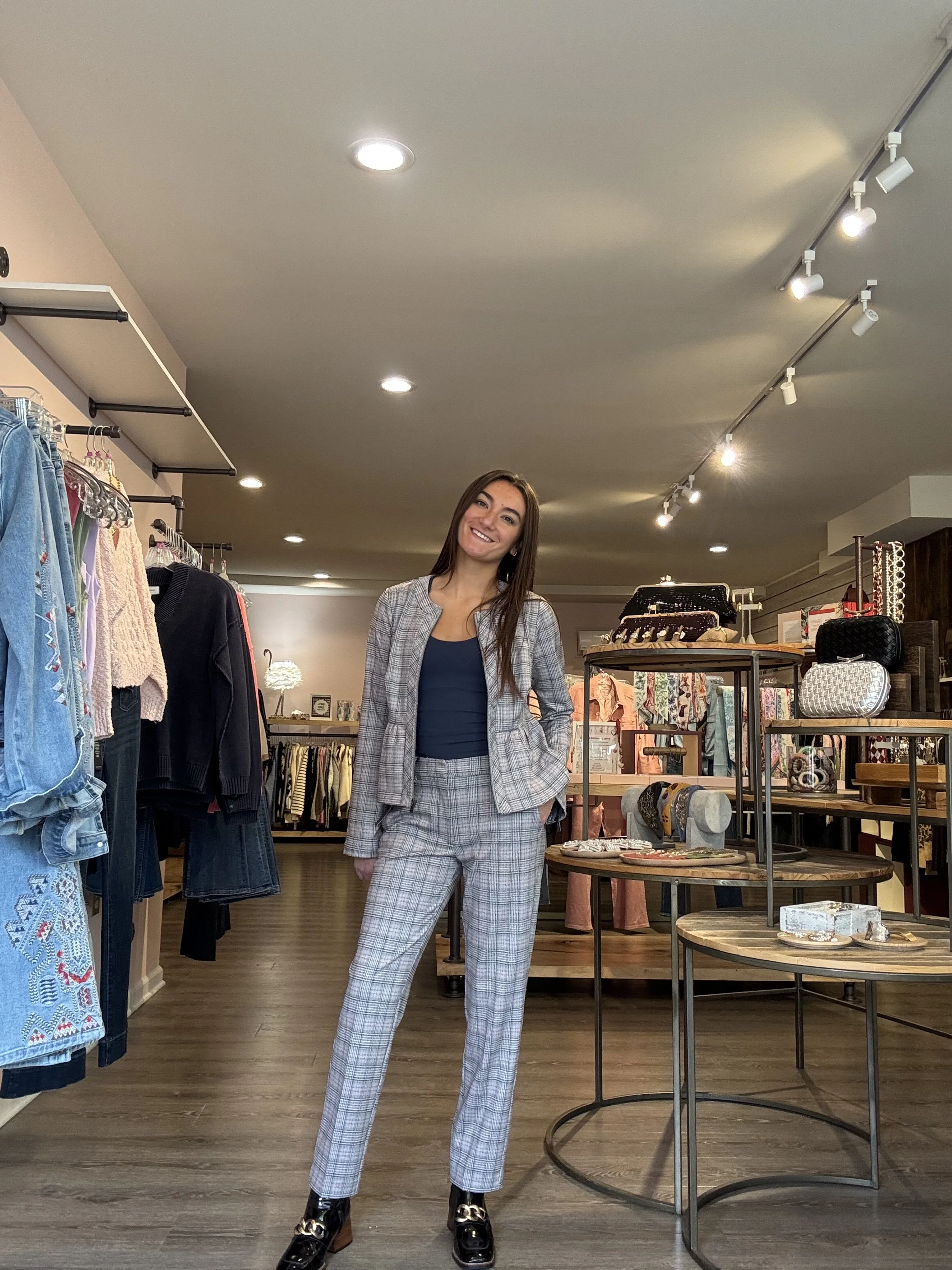 Woman in plaid pants and blazer smiling inside a clothing store.