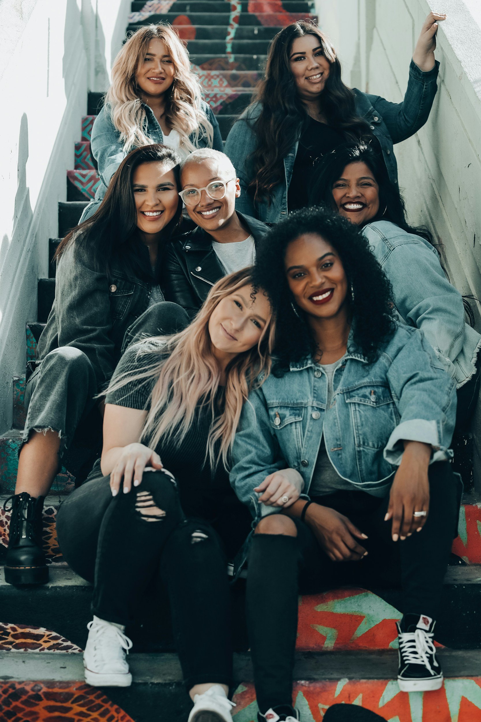 A diverse group of eight women sitting on a decorated staircase, smiling and posing for the photo.