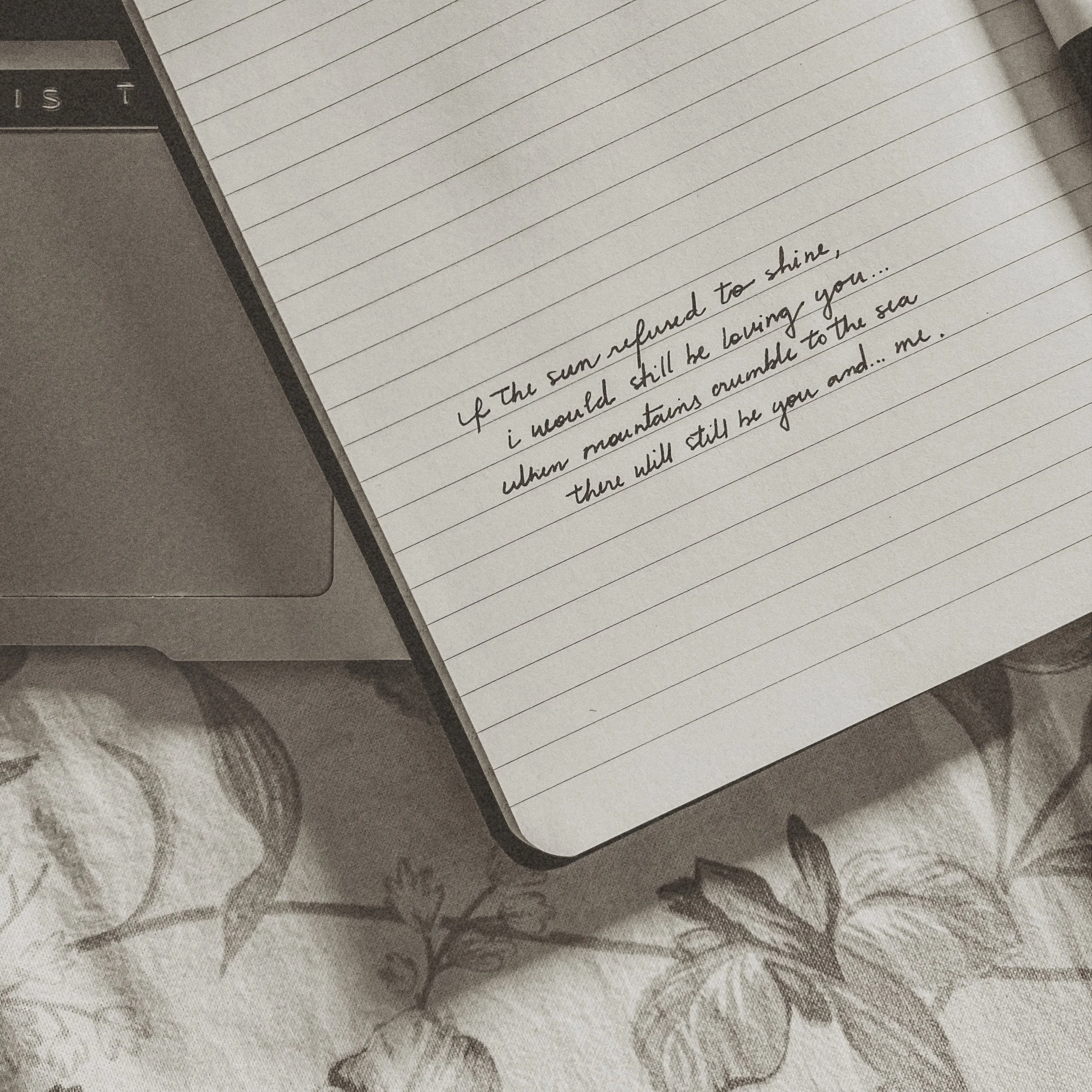 Open notebook with handwritten lyrics beside a laptop on floral bedding. A soft, nostalgic image of love and memory.