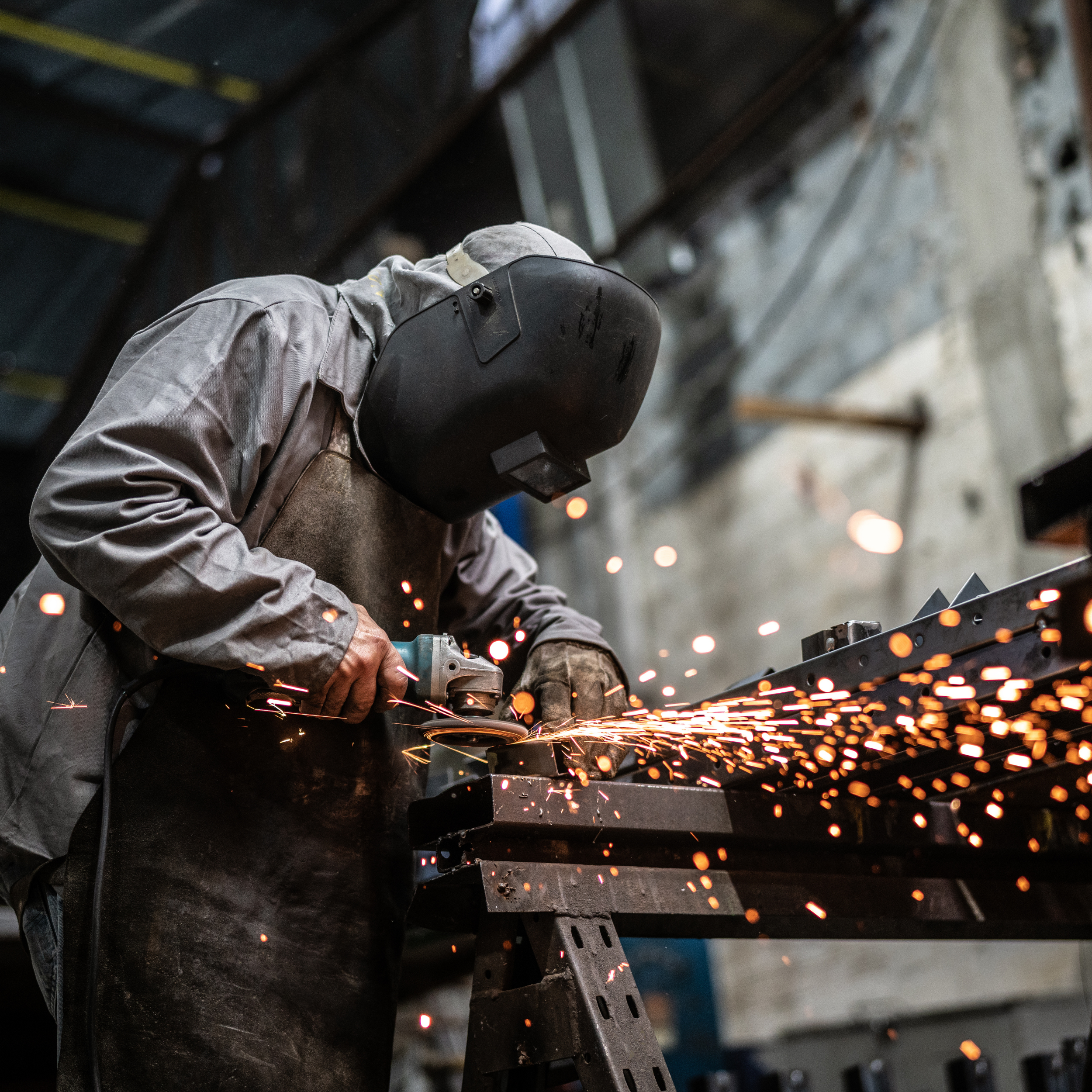 A worker wearing a welding helmet and protective gear welding metal, sparks flying in a workshop.