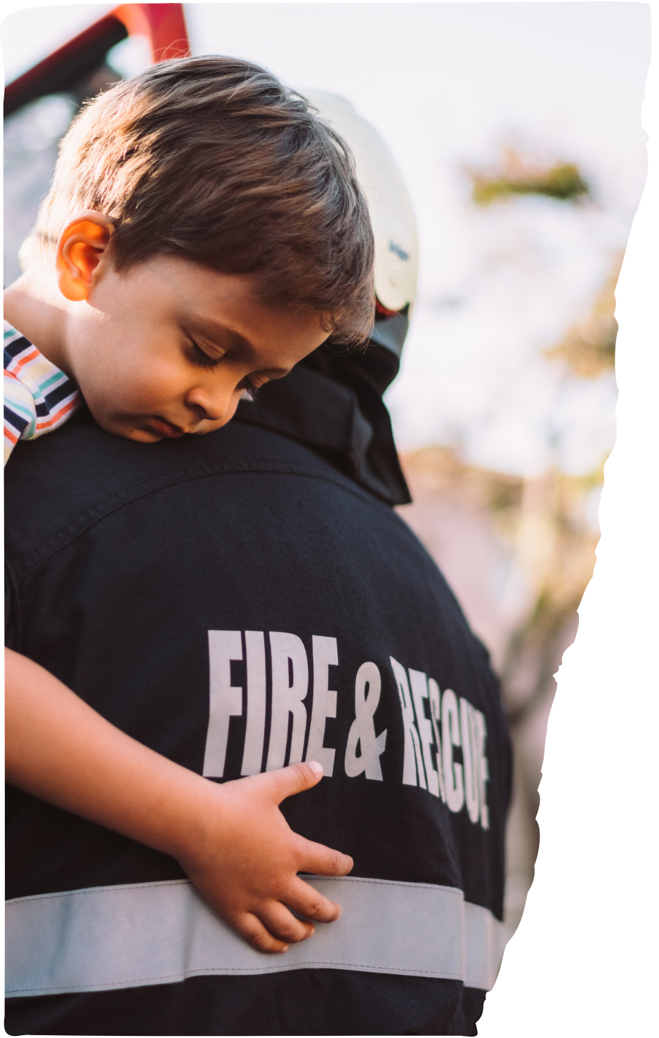 A young boy is sleeping on the shoulder of a firefighter in uniform during daytime.