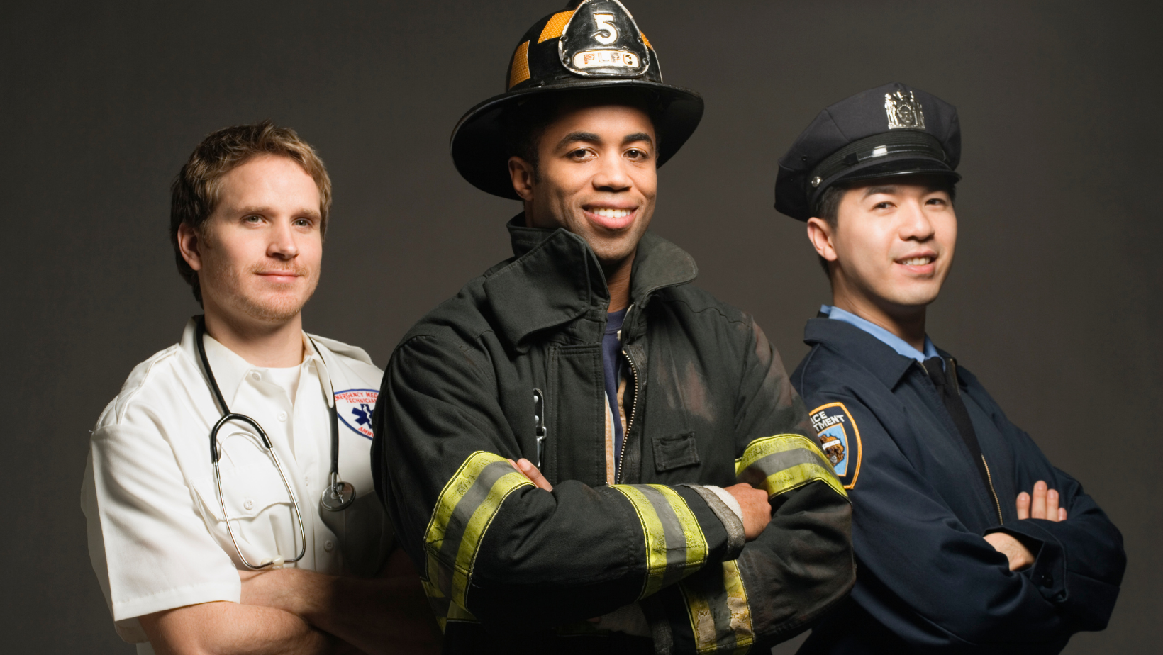 Three professionals standing side by side with arms crossed: a male doctor with stethoscope, a male firefighter in uniform with helmet, and a male police officer in uniform with hat, posing confidently against a dark background.