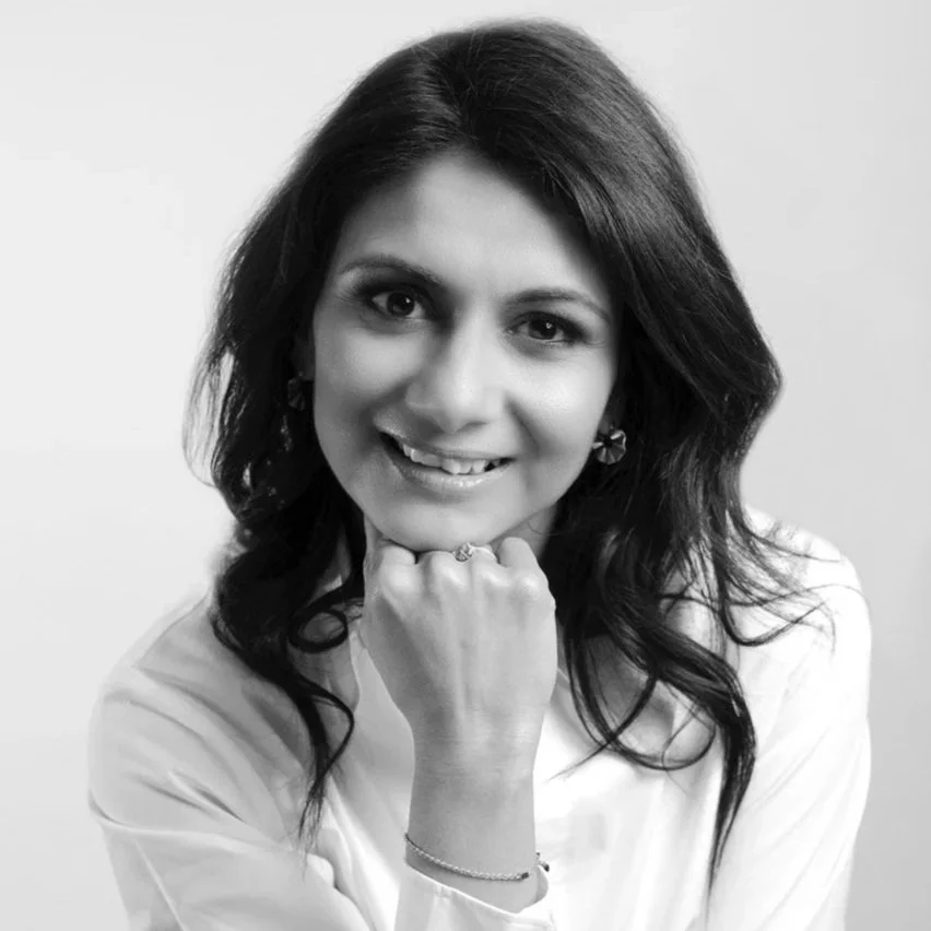 Black and white photo of a woman with dark hair, smiling, resting her chin on her fist, wearing earrings and a light-colored blouse.