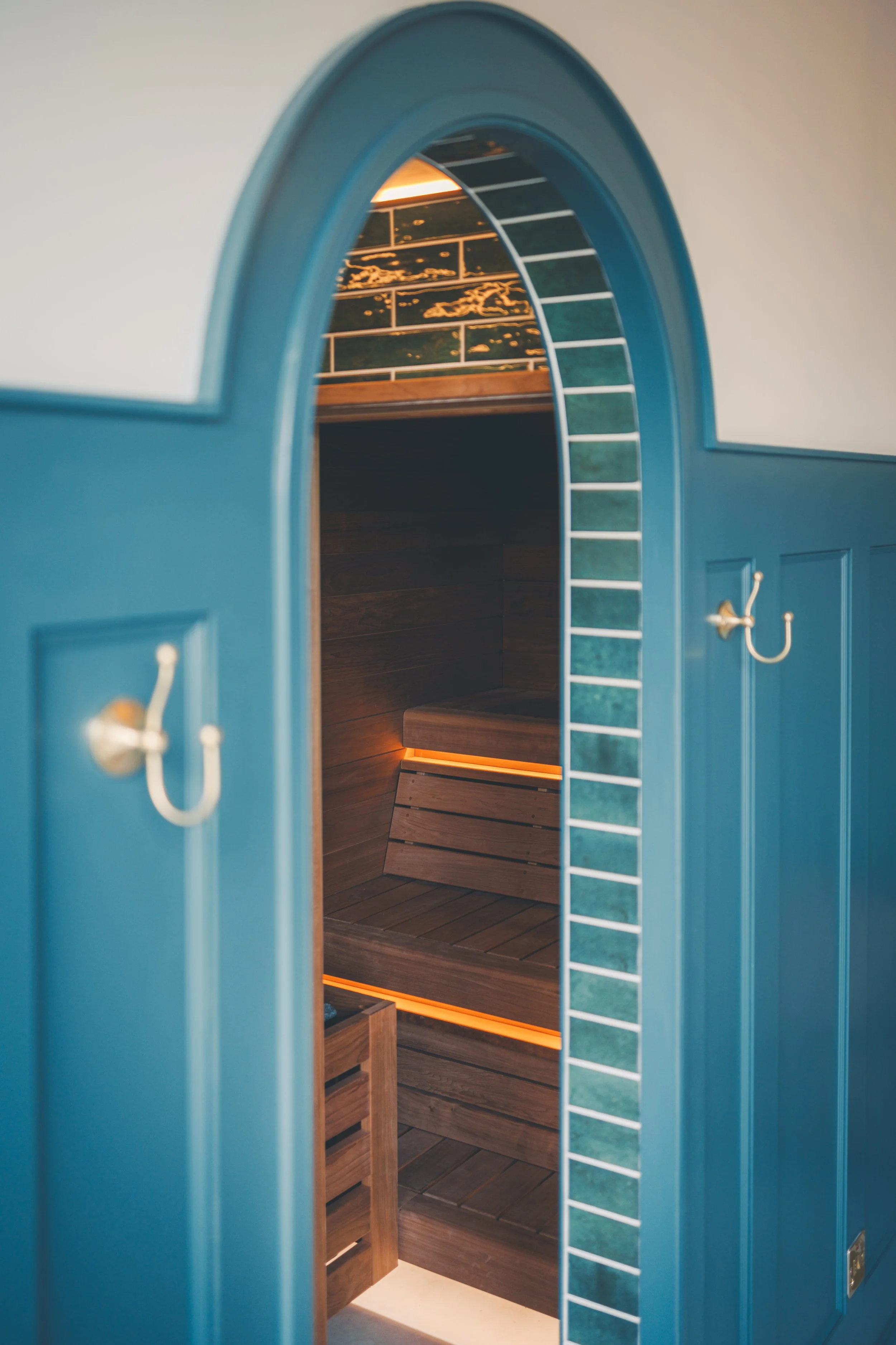 View of a sauna room through a blue arched doorway with hooks on the wall.