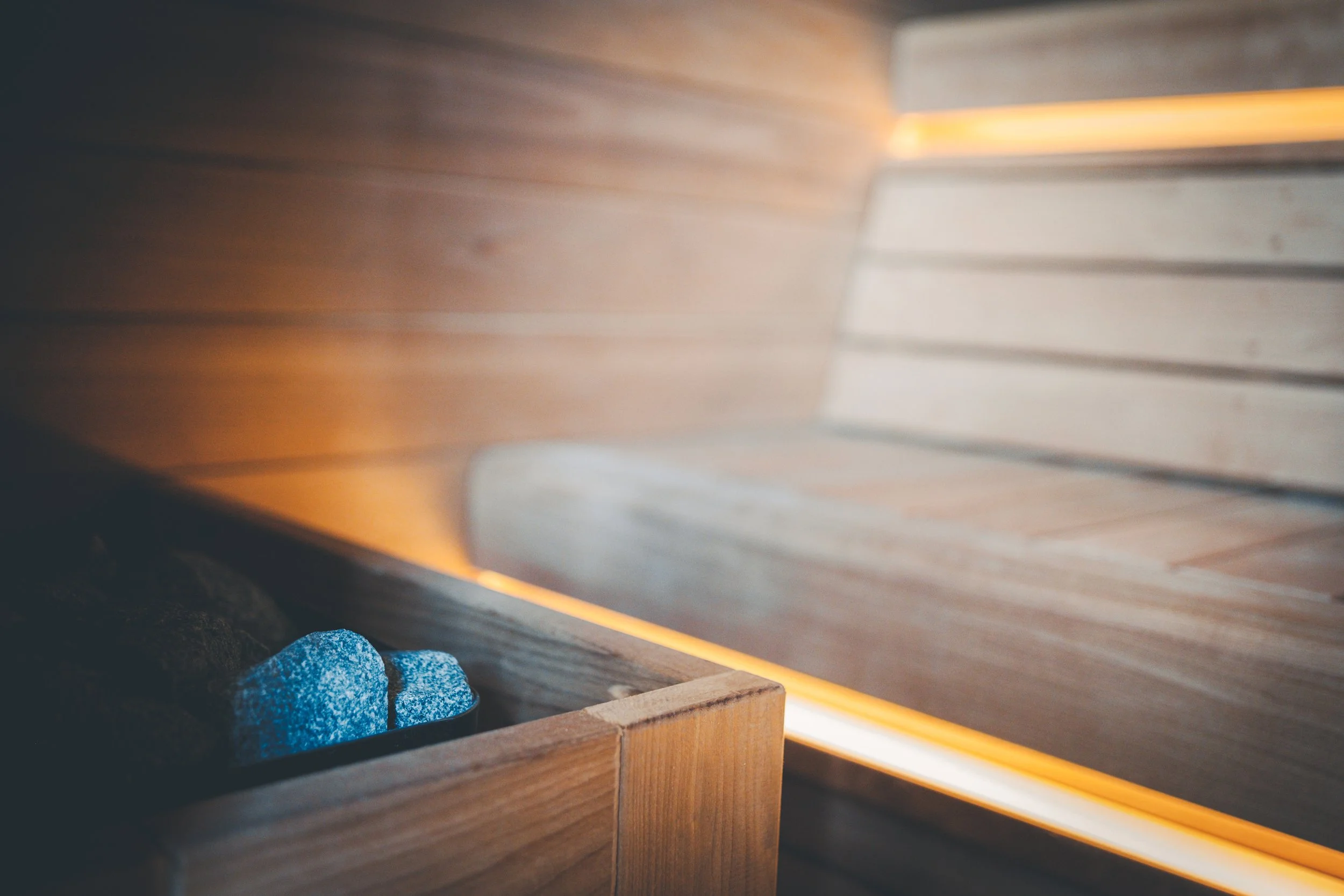 Close-up of a wooden box with glowing blue stones inside, underneath a piece of smooth wood or metal, with a warm light reflecting on a wooden surface.