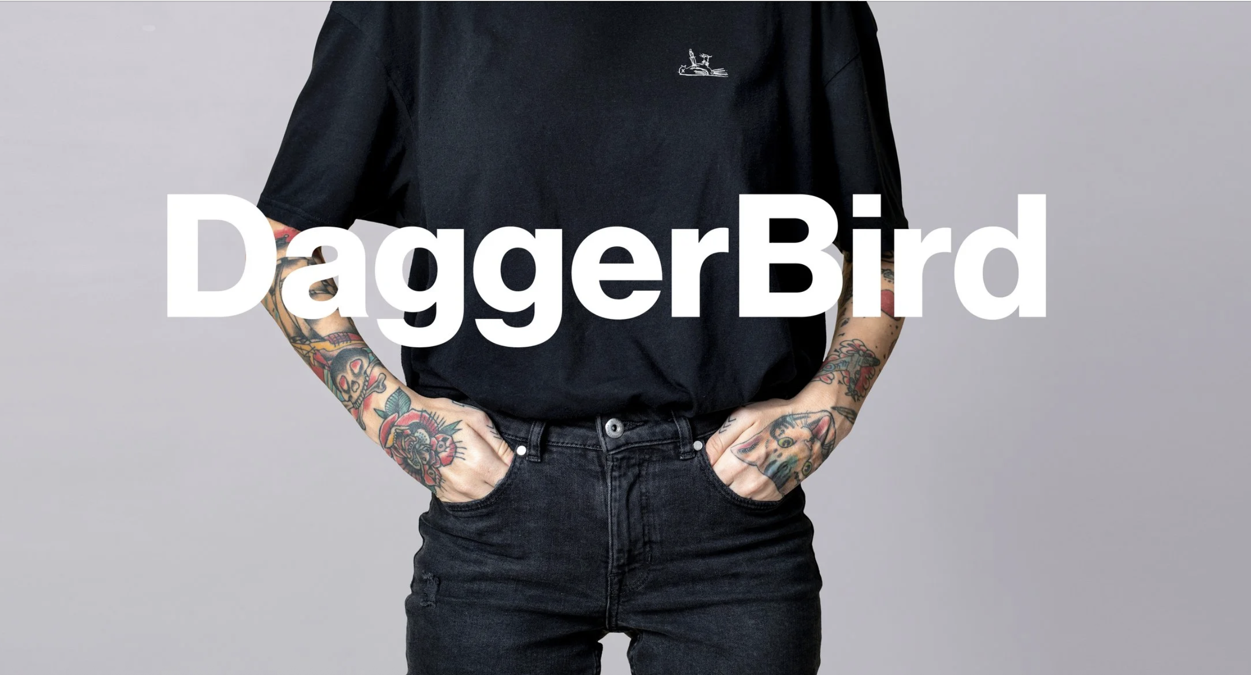 A person wearing a black t-shirt and black jeans with tattoos on both arms, standing against a gray background, with the text 'DaggerBird' overlaid.