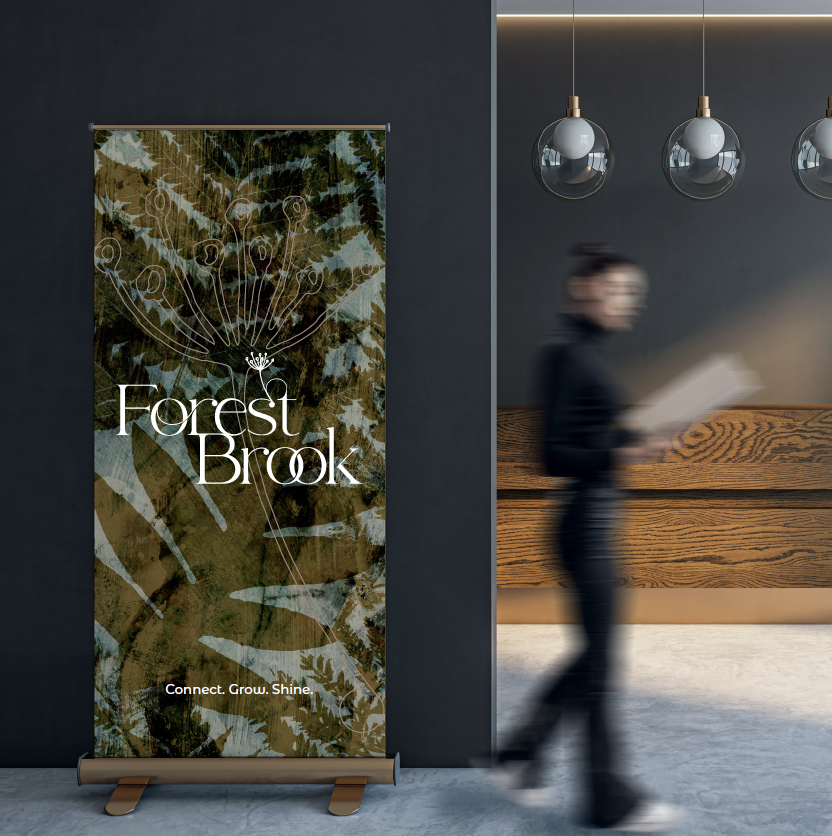 Interior with Forest Brook vertical banner, dark wall, woman walking past holding a tablet, wooden reception desk, hanging spherical pendant lights.