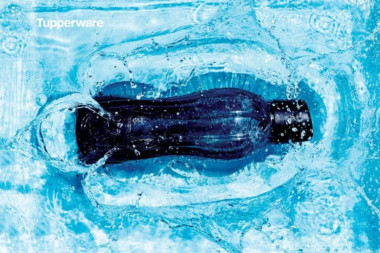 Black Tupperware bottle floating and splashing in water.