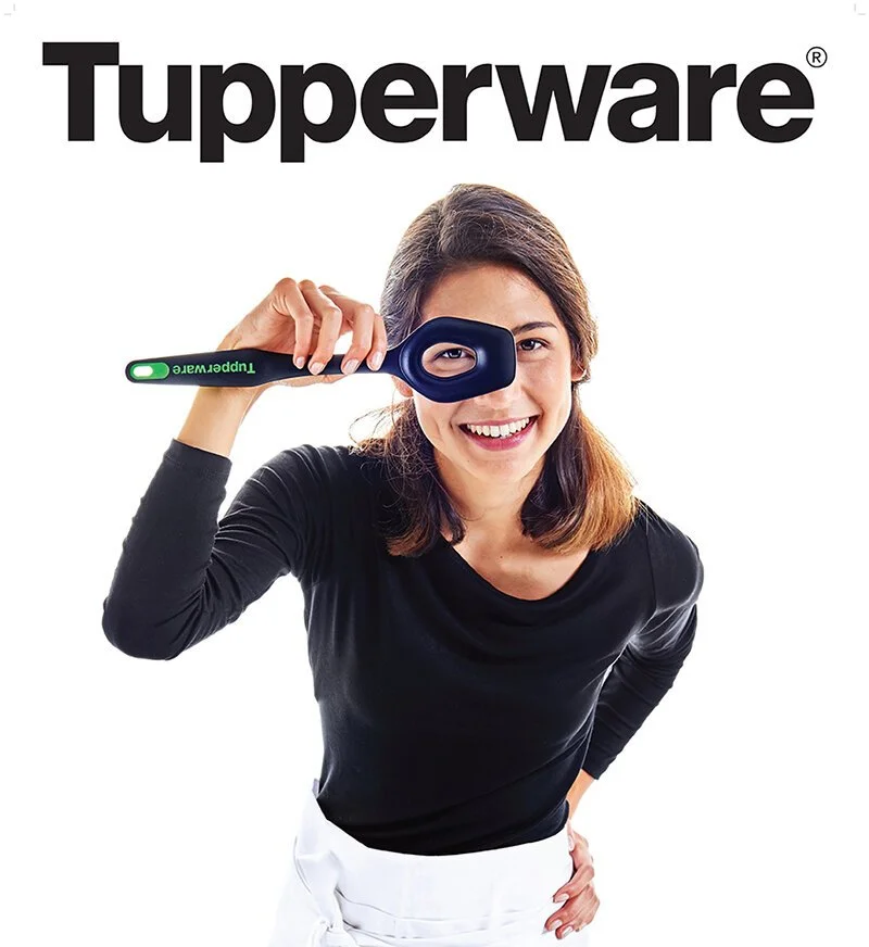 Woman smiling and holding a Tupperware spatula with her eye