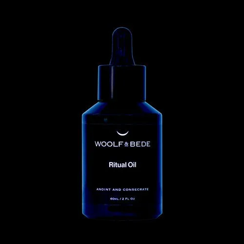 Dark blue bottle of Wool & Bede Ritual Oil with a dropper cap, illuminated against a black background.