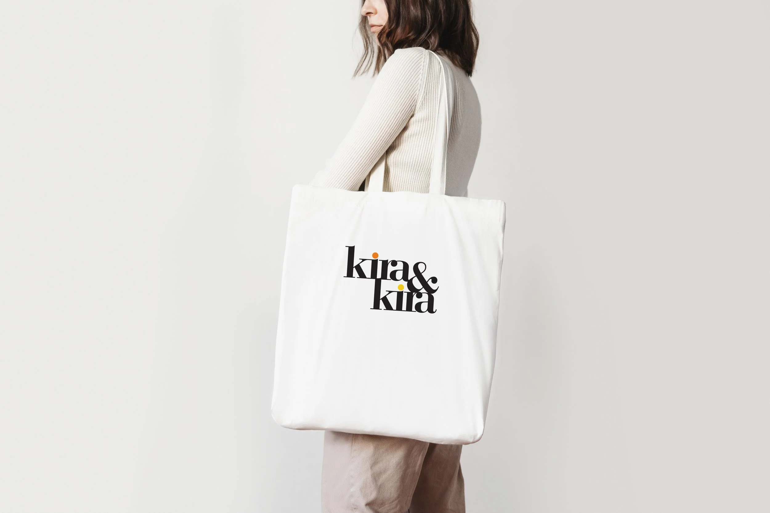 A woman holding a large white tote bag with the text 'kira&kira' printed in black on it.