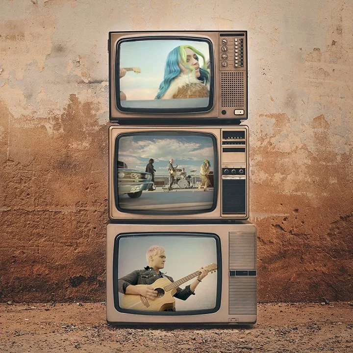 Stacked vintage televisions showing scenes of people and a musician with a guitar, set against a rough wall.
