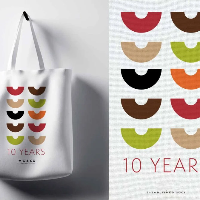 White tote bag with colorful half-circle patterns arranged in a grid and the text '10 YEARS' below.