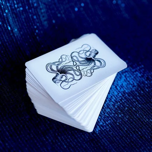 A deck of playing cards with a detailed illustration of a tangled snake on the top card, placed on a shiny blue surface.