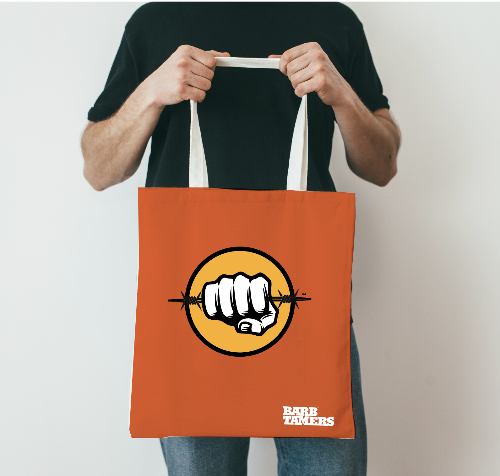 Person holding an orange tote bag with a black and white fist gripping barbed wire logo and the text 'BAB TAMERS' printed in white at the bottom right corner.