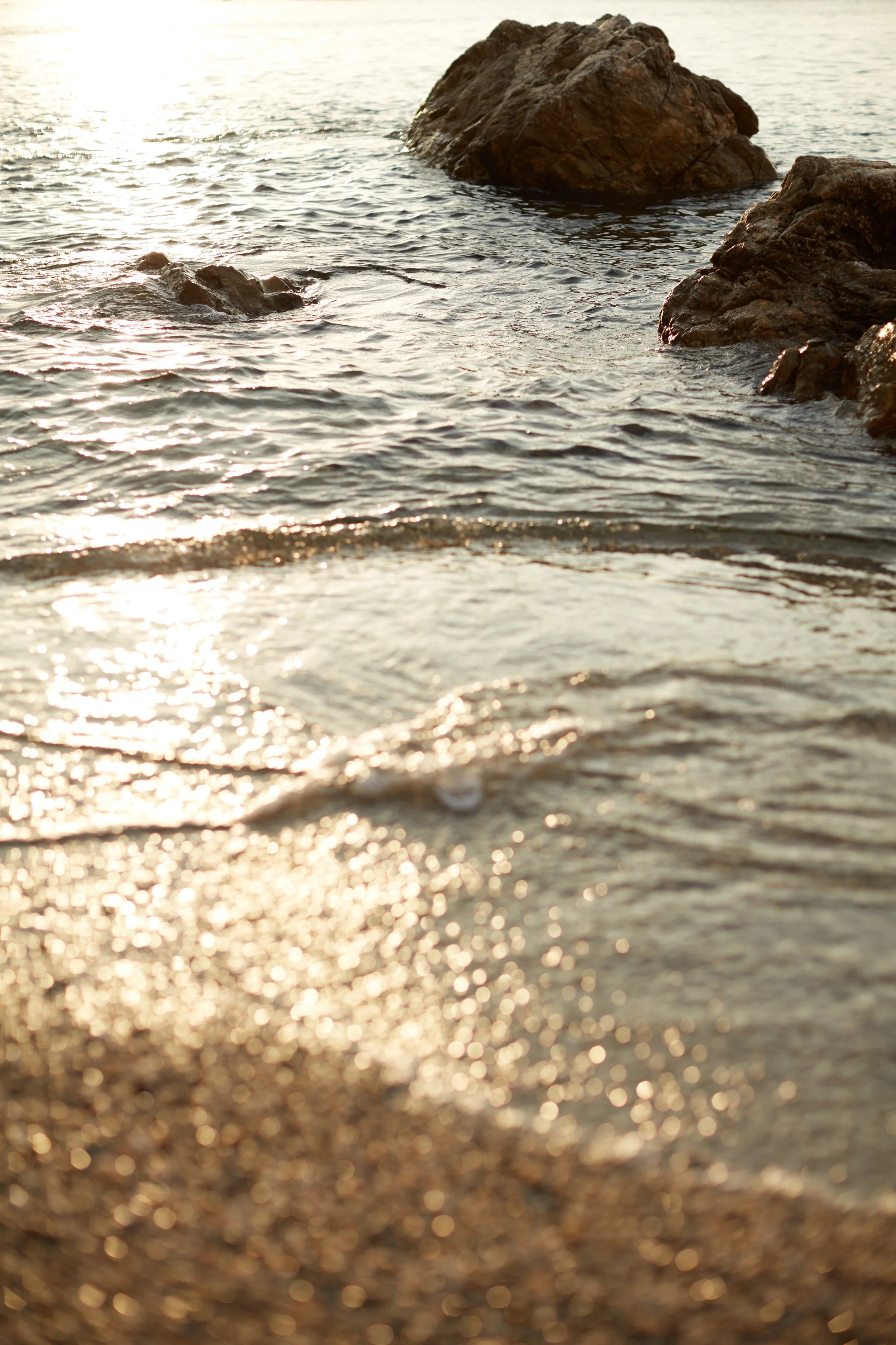 Beach with small rocks and water, illuminated by sunlight.