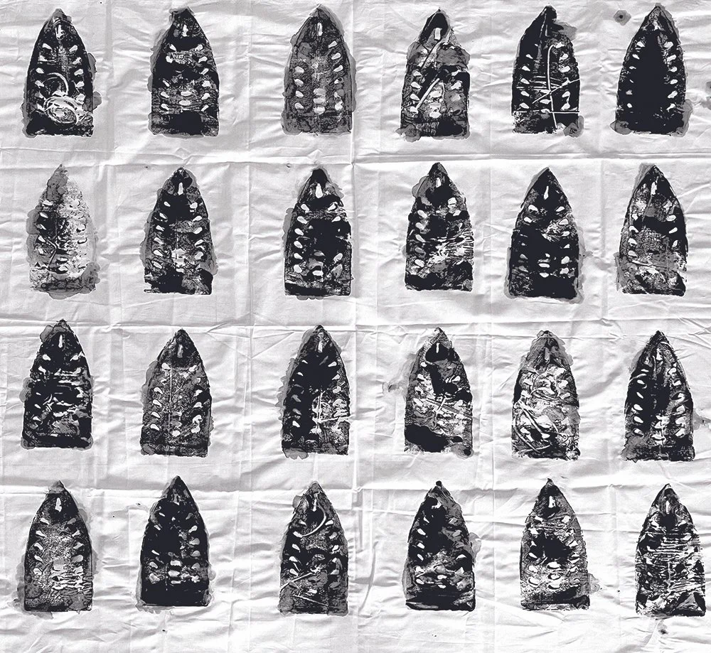 Collection of 24 black and white prehistoric arrowheads arranged in rows on crinkled white paper.