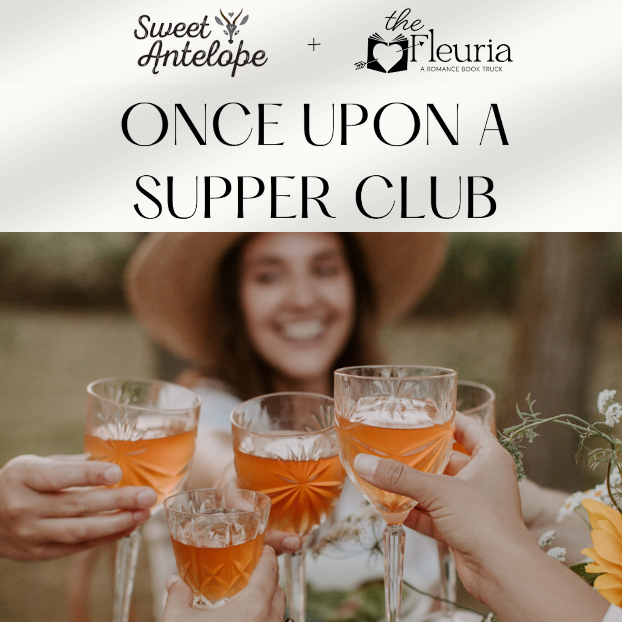 A group of women celebrating outdoors with glasses of orange-colored drinks, smiling, with a woman in a wide-brimmed hat in the background and flowers on the table.