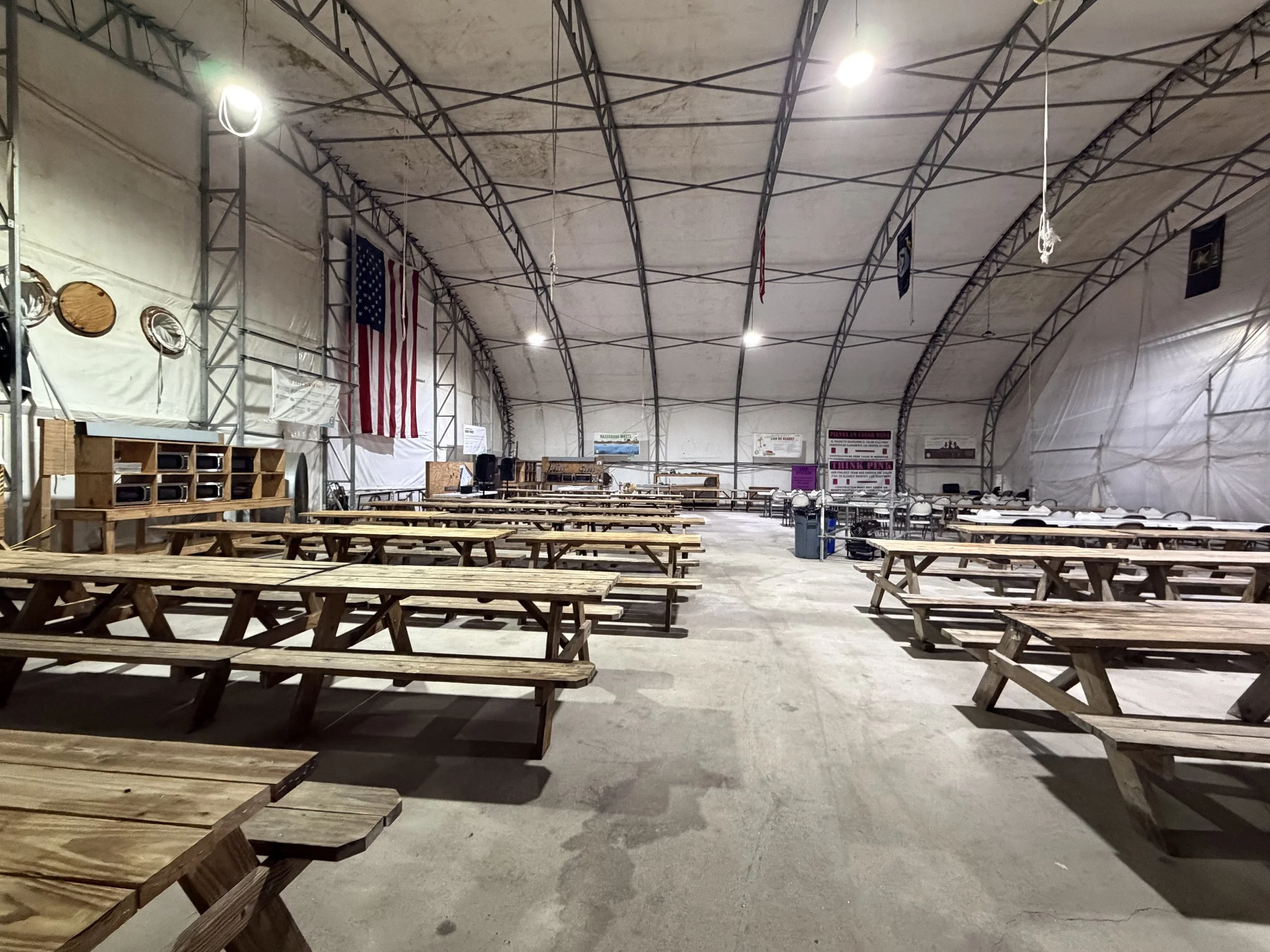 Empty indoor event space with wooden picnic tables and benches, American flags, banners, and a stage area at the far end.Cleaning services