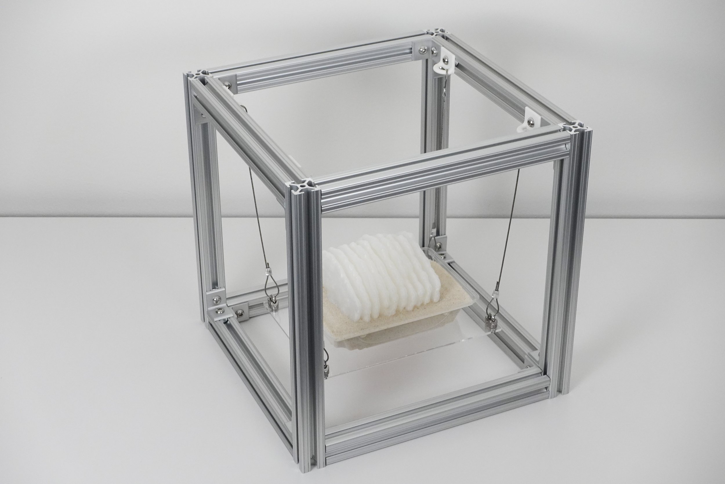 Plastimurus Stratum, 2025. 3D printed polylactic acid, recycled polyethylene terephthalate, aluminum extrusion, steel cable, acrylic, sand, 12 x 12 x 12 in.