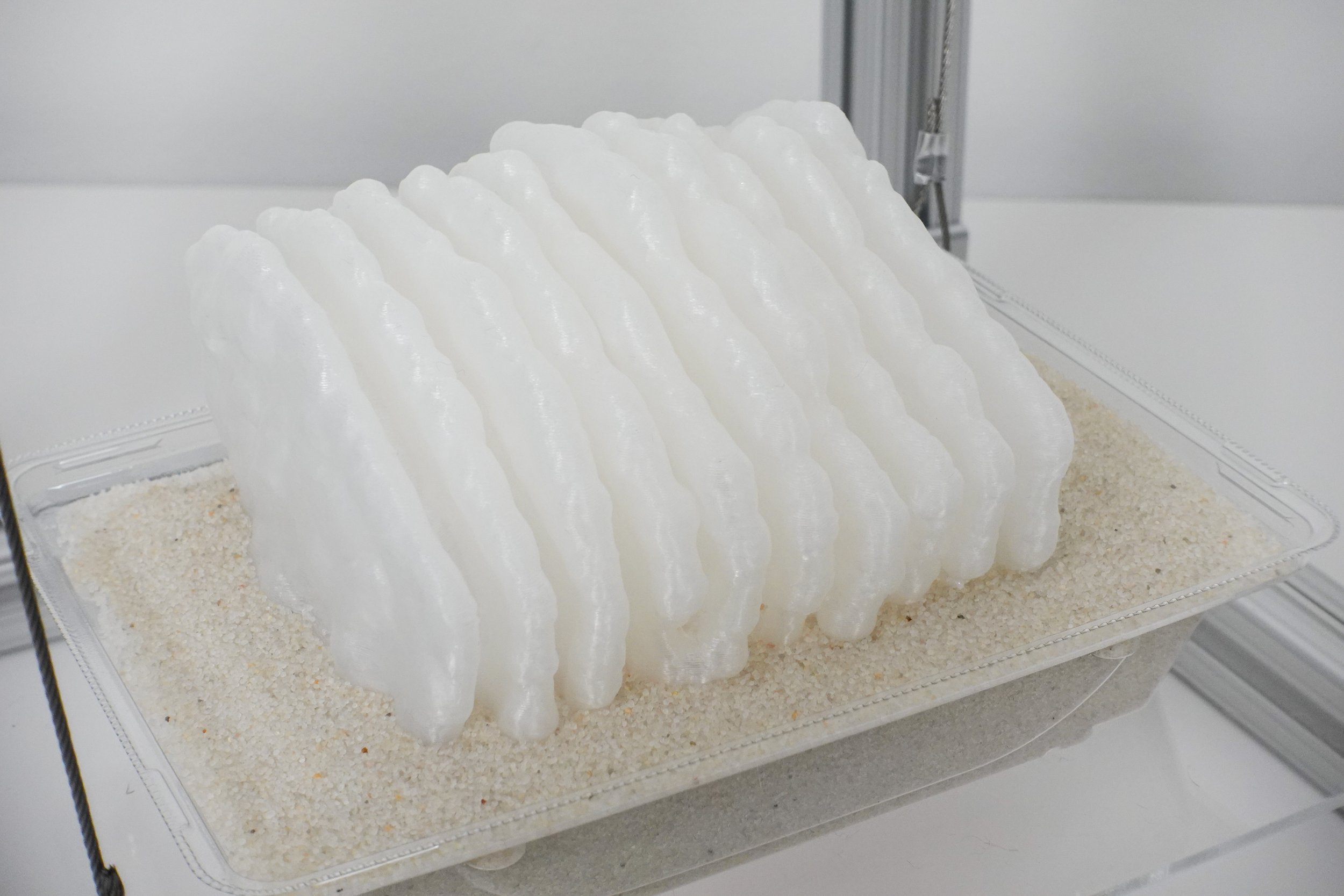 Plastimurus Stratum, 2025. 3D printed polylactic acid, recycled polyethylene terephthalate, aluminum extrusion, steel cable, acrylic, sand, 12 x 12 x 12 in.