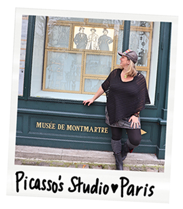 A woman posing in front of a window display at the Musée de Montmartre in Paris. The window features artwork and a sign with the museum's name. The photo has a handwritten caption reading "Picasso's Studio ❤️ Paris."