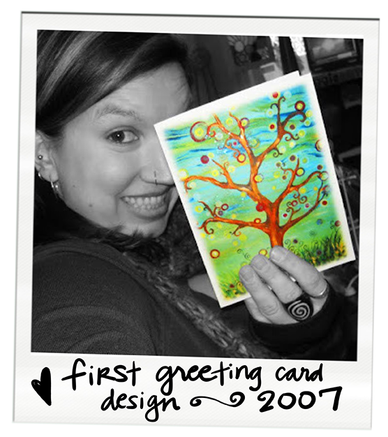 A young woman smiling and holding a colorful greeting card with a whimsical tree design, partially covering her face, in a black and white photo with handwritten text "first greeting card design 2007" at the bottom.