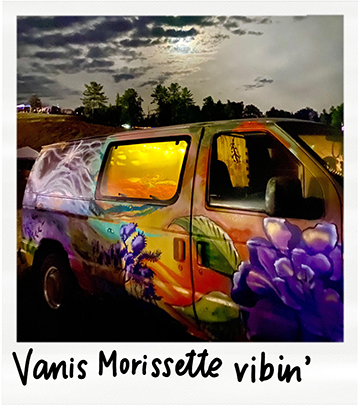 A painted van with colorful floral artwork parked outdoors during cloudy weather at sunset. The image has a caption reading "Vanis Morissette vibin'".