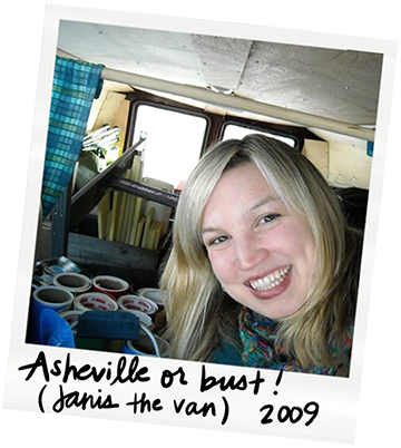 Close-up of a smiling woman with blonde hair inside a van filled with books and cans, with a handwritten note at the bottom that says 'Asheville or bust! Jani the van 2009.'
