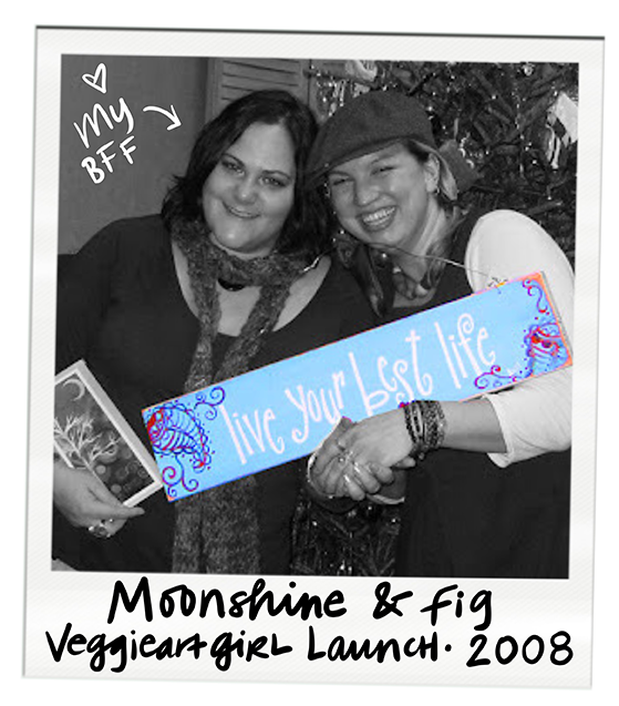 Two women smiling at a photo booth, one holding a book or magazine, with handwritten notes and a colorful sign that says 'Live your best life.' The photo is black and white, with a hand-drawn heart and note that says 'My BFF.' The bottom text reads 'Moonshine & fig Veggieartgirl Launch 2008.'