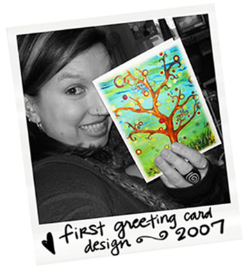 A woman holding a colorful drawing of a tree with orange branches, multicolored circles, and a green grassy background.
