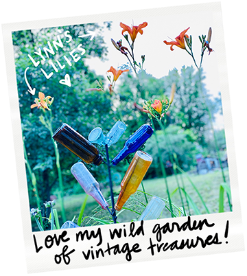 Collection of vintage glass bottles arranged on a wire plant stand in a garden, with lilies and greenery in the background, featuring handwritten notes and captions.