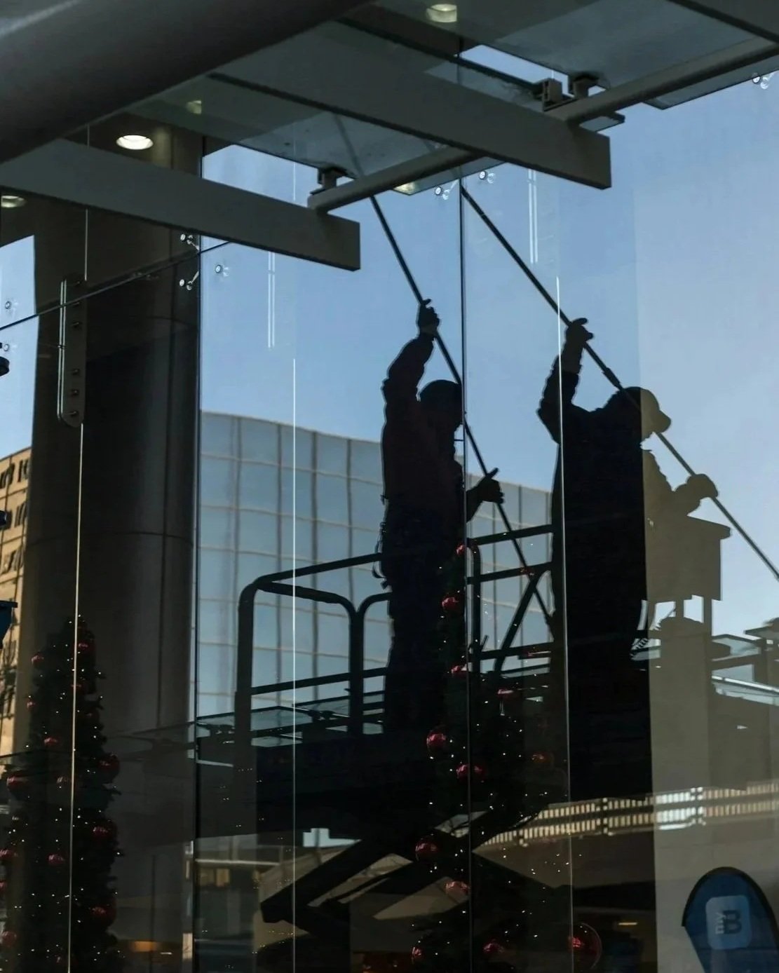 Reflection of commercial cleaning workers cleaning large glass windows inside a building during daytime