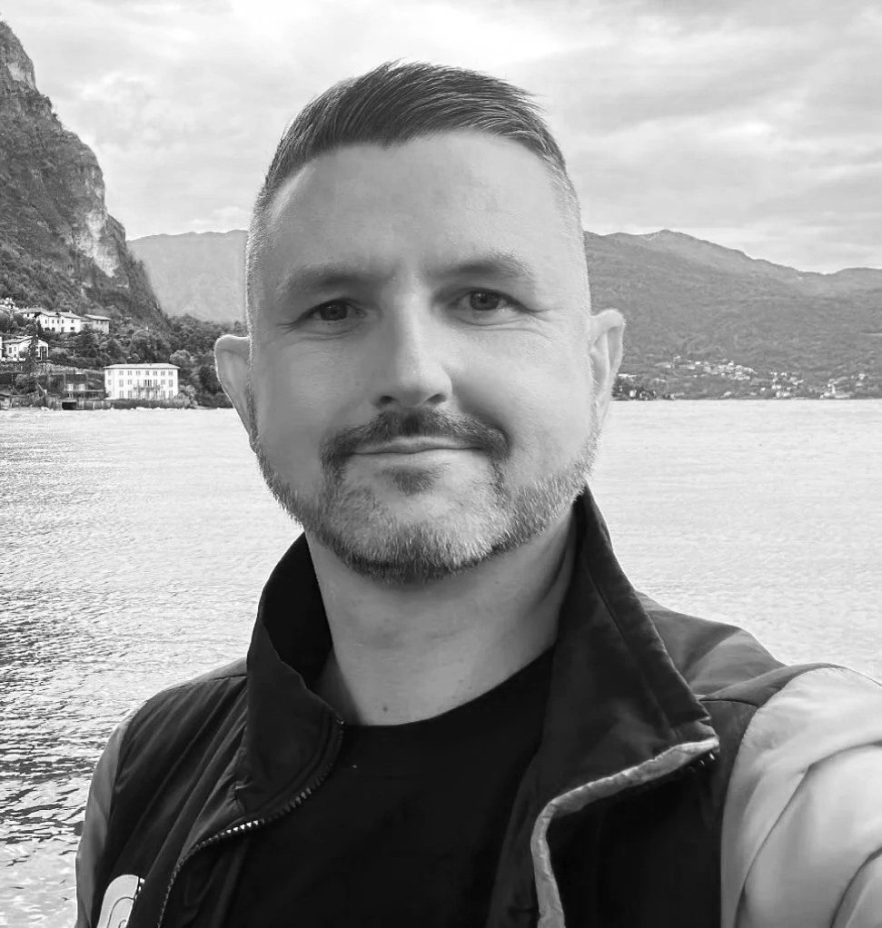 A man taking a selfie near a body of water with mountains in the background